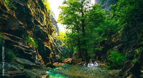 People camping in a narrow valley surrounded by trees and river flowing in the middle. An image from Wadi Lajab, Saudi Arabia photo