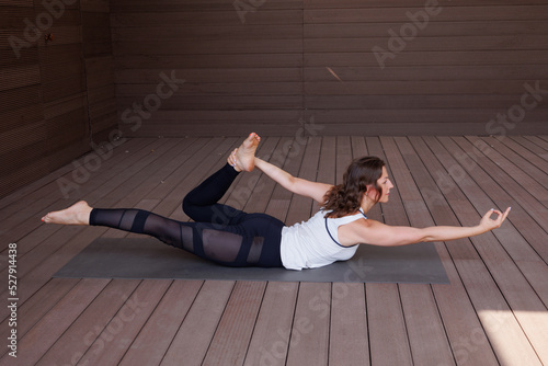 Beautiful strong muscular woman doing stretching on mat on terrace outdoors. Healthy young adult girl in sportswear stretch alone. Fit thin gimnast doing yoga, training on mat