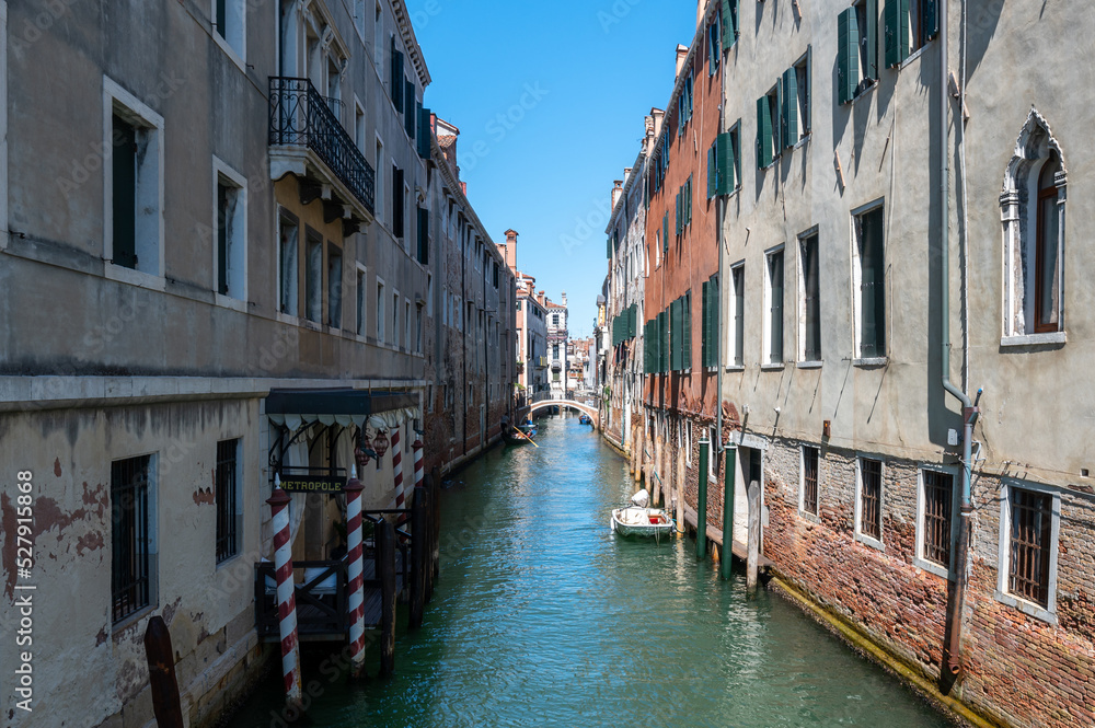 Vue typique d'un canal a Venise avec les reflets, les bateaux et un pont sur fond de ciel bleu