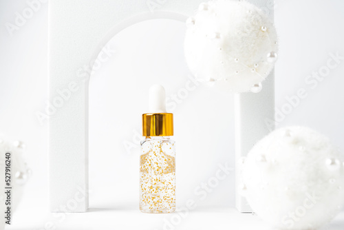 transparent bottle with beauty serum, hyaluronic acid, 24k gold and vitamins in a arch with new year decorations. Home face and body care concept photo