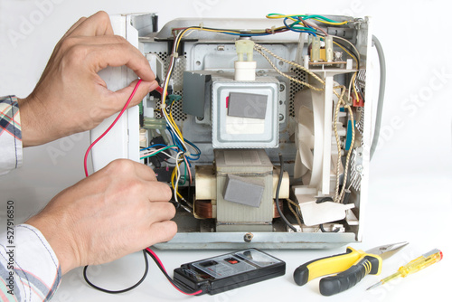 Repair of a microwave oven. The master measures the voltage with a tester, on a white isolated background photo