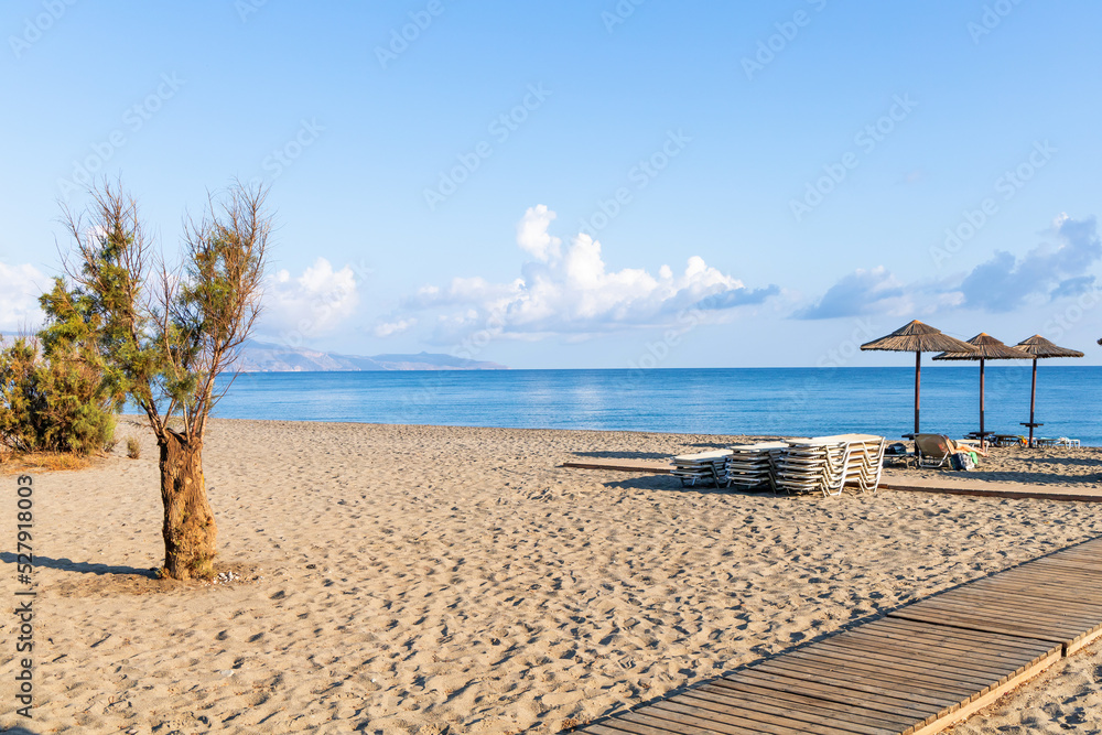 Empty beach with sun loungers and umbrellas in the early morning on a sunny day on the Crete island Greece. . High quality photo
