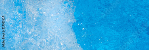 Surface of blue swimming pool water with light reflection, splashes and waves. Texture of transparent blue water with waves in swimming pool. Trendy abstract nature background. long banner.