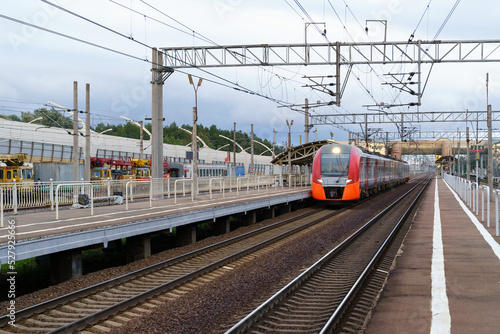 Front view of modern russian intercity high speed passenger train on railroad at sunset, autumn forest and station platform on background. Commercial suburban railroad transportation concept