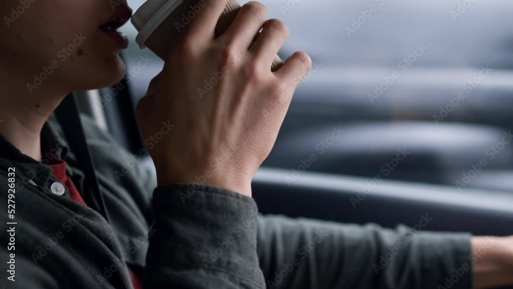 A male driver is driving in a car drinking coffee. The driver drinks coffee while driving. Close-up of man male driver in car movement on motorway track
A male driver is driving in a car drinking coffee. The driver drinks coffee while driving. Close-up of man male driver in car movement on motorway track