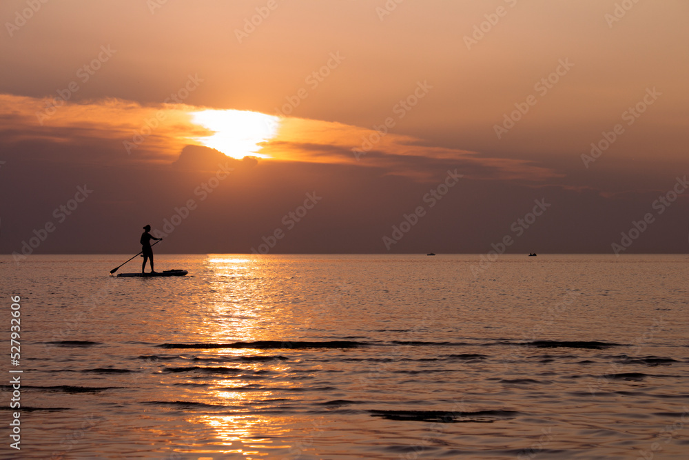 A woman on a sup board with an oar floats on the sea