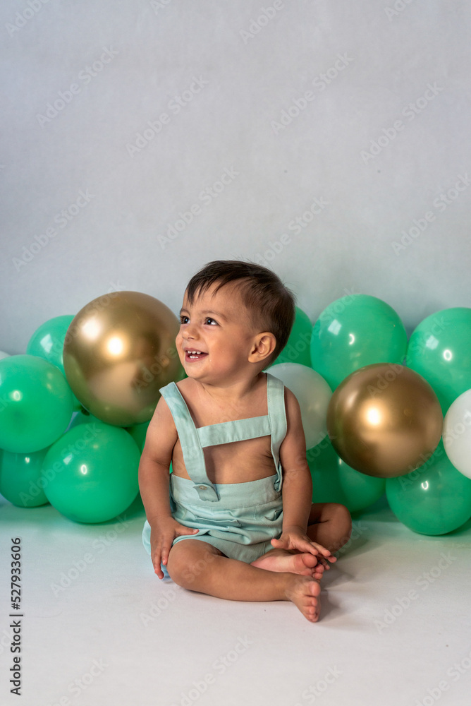 Cheerful baby boy sitting near balloons in studio Cheerful baby boy sitting near balloons in studio