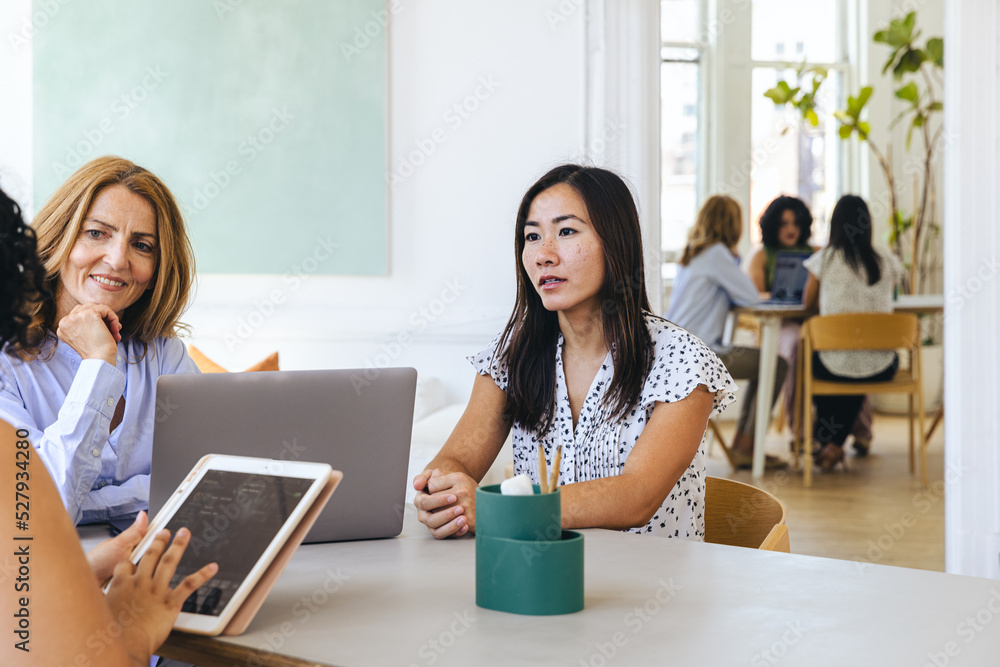Businesswoman holding ipad discussing strategy with female colleagues Businesswoman holding ipad discussing strategy with female colleagues