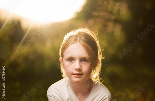 Young Caucasian female looking straight into camera with the sun on her back outdoors.