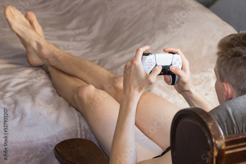Young man holding in his hands Play Station 5 Dual Sense controller and playing video games on gaming console at home.