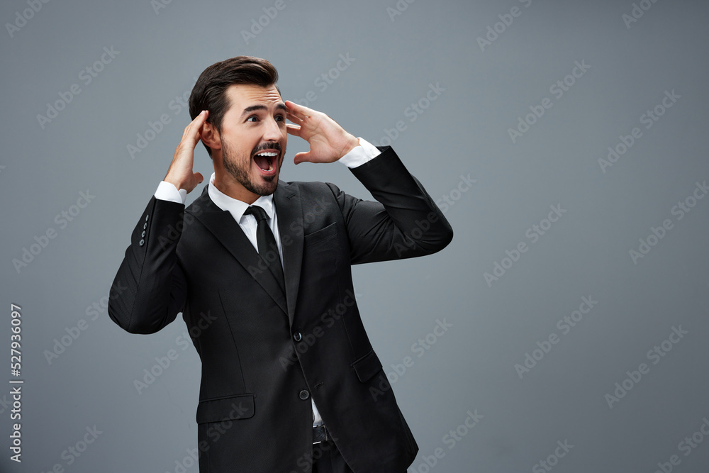 Man businessman surprised smile with teeth and raised his hands up happy in a business suit on a gray background with a brunette beard Man businessman surprised smile with teeth and raised his hands up happy in a business suit on a gray background with a brunette beard