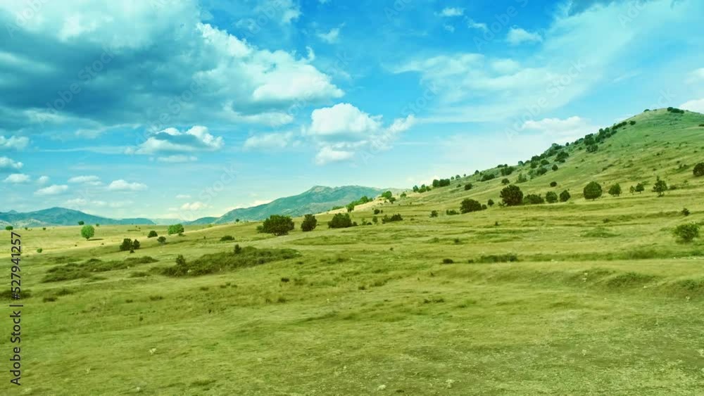 Lateral drone motion view along gentle slope, uneven grass covered terrain and cloudy sky Lateral drone motion view along gentle slope, uneven grass covered terrain and cloudy sky