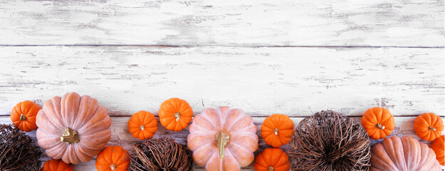Fall bottom border of pumpkins and natural decor over a rustic white wood banner background. Above view with copy space.