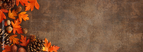 Colorful fall leaves, nuts and pine cones. Corner border over a rustic dark banner background. Overhead view with copy space. #527942211