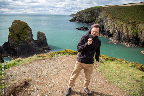 Caucasian hiker man taking photos with an action camera on the top of a hill in Nohoval Cove, County Cork, Ireland photo