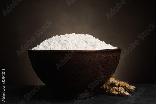 Wheat flour in bowl and spikes on black table