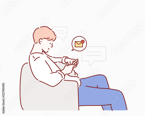 The young man is sitting on the sofa checking the message on his cell phone. Hand drawn style vector design illustrations.