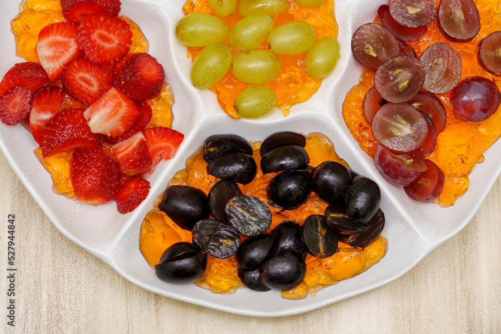 flatten view of a tray with fresh grapes of different colors and halved strawberries on orange jelly flatten view of a tray with fresh grapes of different colors and halved strawberries on orange jelly
