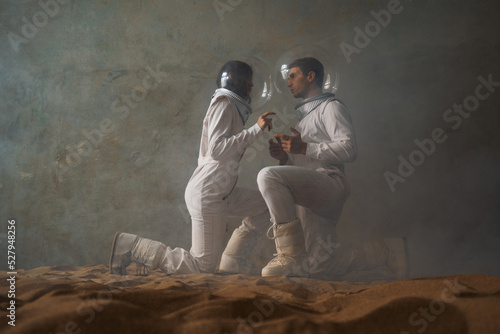 Astronauts on a deserted planet, a man and a woman in white spacesuits with large glass helmets sit and talk, Melancholy in space © Ulia Koltyrina