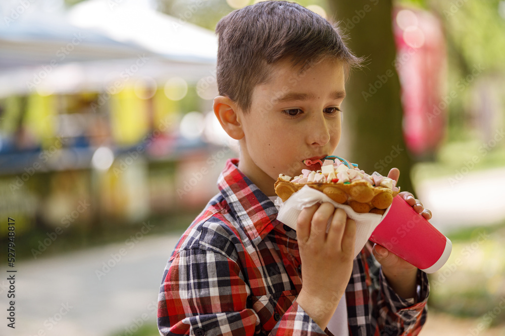 Small Caucasian boy eating sweet waffle at street. Child with fast food in hands. Small Caucasian boy eating sweet waffle at street. Child with fast food in hands.
