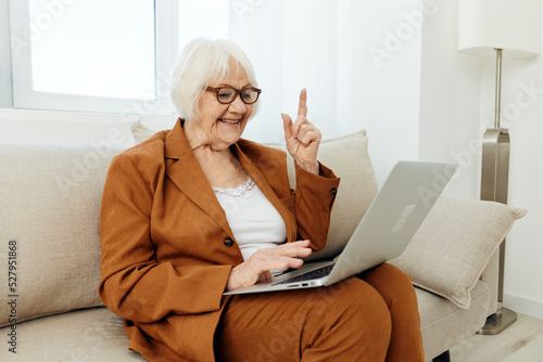 an experienced, elderly woman is sitting on a sofa in a brown suit, holding a video conference on a laptop, passing on her knowledge to a new generation