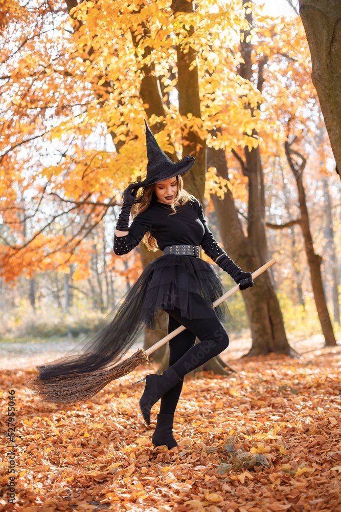 Naklejka premium Woman in witch costume standing in autumn forest on Halloween