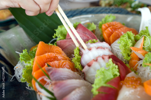 Closeup tako picking with chopsticks from mix sashimi set in ceramic plate. Japanese Cuisine Buffet. Chef's Choice: Salmon, hamachi, Tako, Hotate and hokkigai