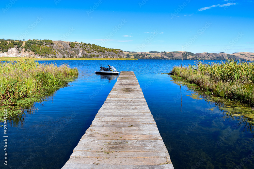 Beautiful lake on a summer day and rustic wooden dock. Montains in blue sky.