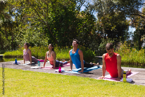 Men and women in sportswear practicing yoga on exercise mats in park