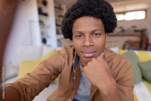 Portrait of african american young man with hand on chin sitting on sofa home