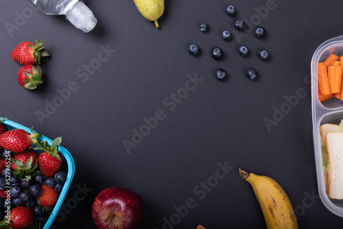Overhead view of healthy food and tiffin box by water bottle over black background, copy space photo