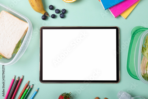 Digital tablet with blank screen by sandwiches, fruits and stationery on green background