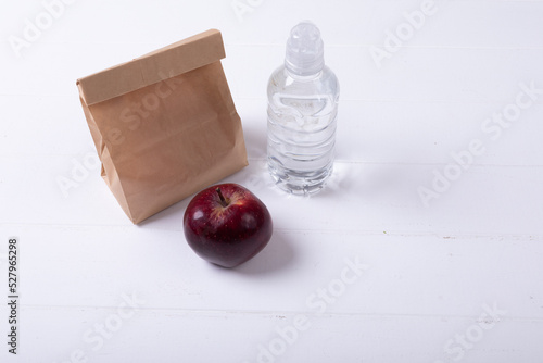 High angle view of apple and paper lunch bag with water bottle on white background