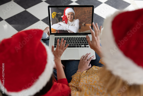 Caucasian woman with her daughter at home at Christmas, using laptop computer, video chatting with a