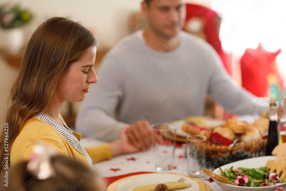 Multi generation caucasian family sitting at table and praying with eyes closed before dinner