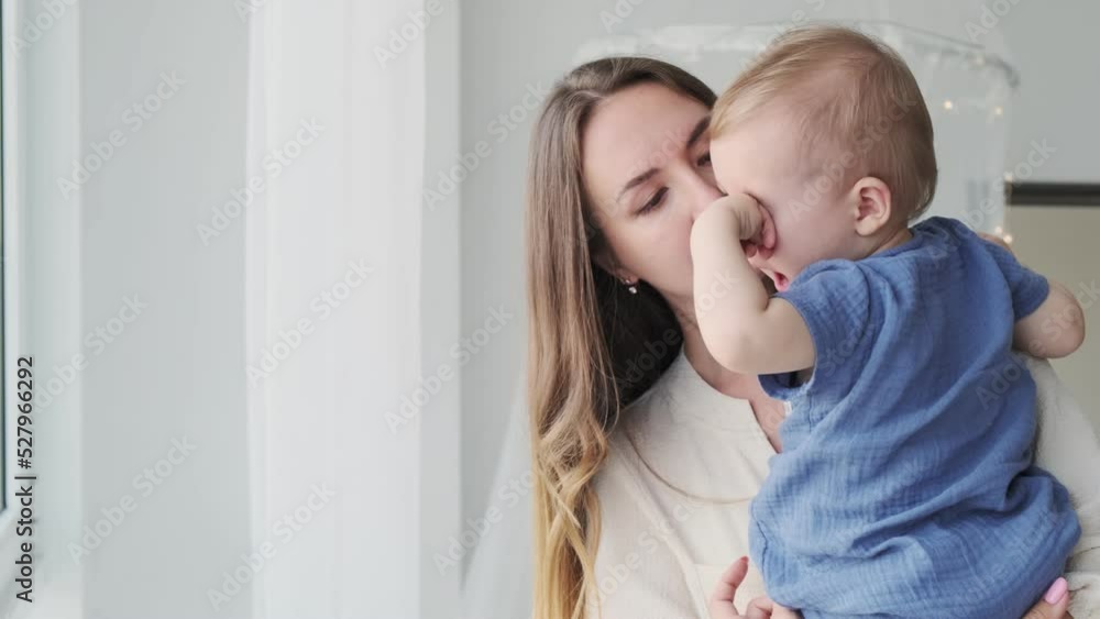 Close-up of a beautiful loving mother in a dress, who is standing at the window with a baby in her arms. The little son rubs his eyes. Happy loving family
Close-up of a beautiful loving mother in a dress, who is standing at the window with a baby in her arms. The little son rubs his eyes. Happy loving family