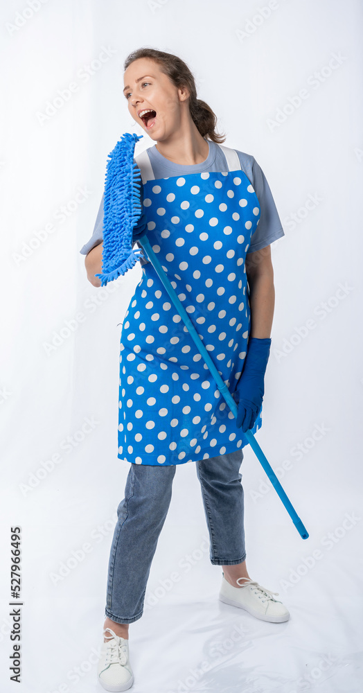european housewife in a kitchen apron, jeans on a white background, full length portrait. a woman holds a mop, sings, dances. cleaning of premises