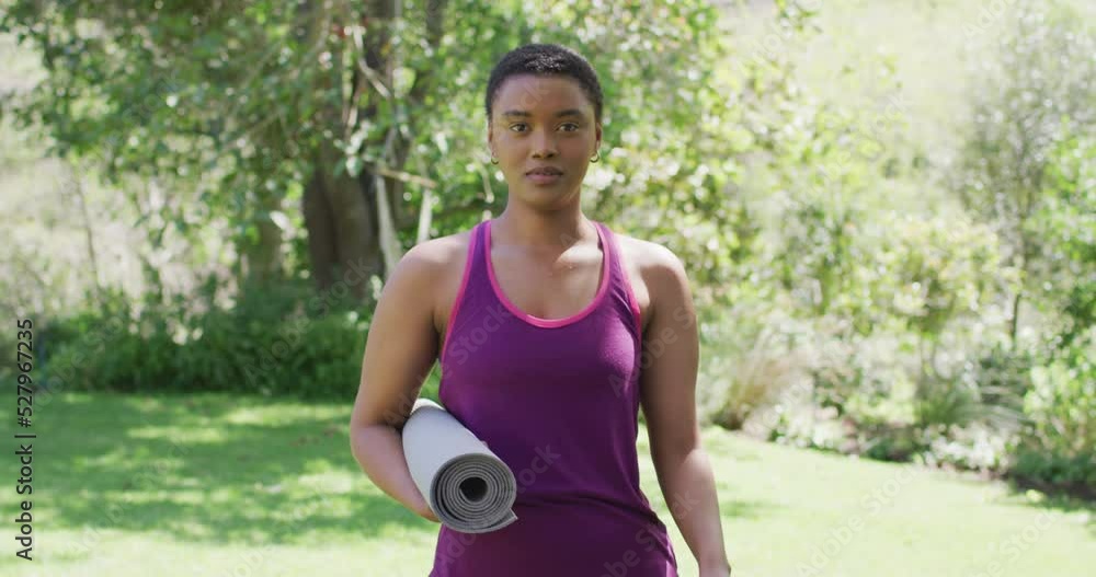 Portrait of biracial woman holding yoga mat laughing outside in garden on a sunny day Portrait of biracial woman holding yoga mat laughing outside in garden on a sunny day