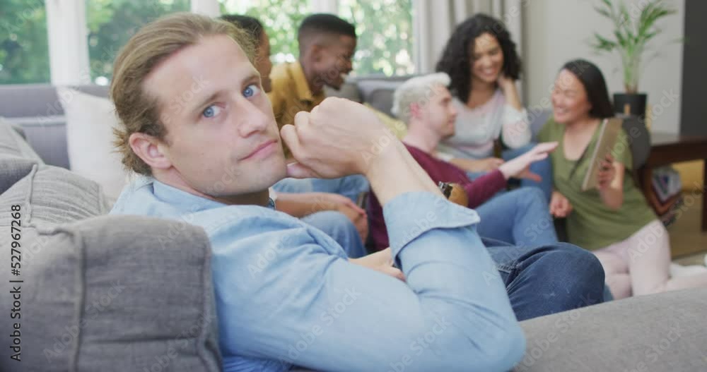 Smiling caucasian man sitting with diverse group of happy friends socialising in living room Smiling caucasian man sitting with diverse group of happy friends socialising in living room