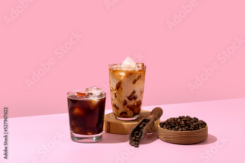 Ice coffee in a tall glass with cream poured over and coffee beans. Set with different types of coffee drinks on a pink table. photo