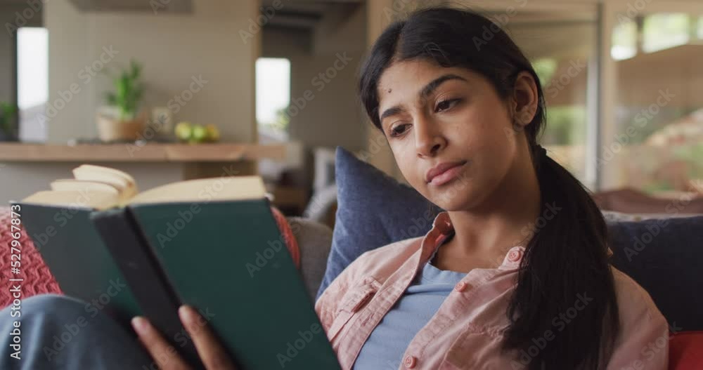 Video of biracial woman sitting on sofa and reading book Video of biracial woman sitting on sofa and reading book