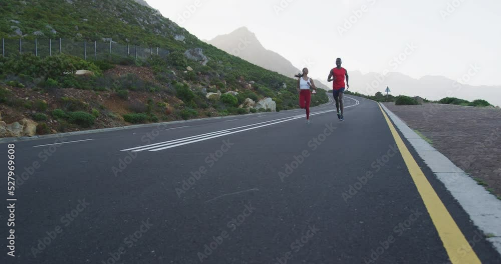 Diverse fit couple exercising running on a country road near mountains Diverse fit couple exercising running on a country road near mountains