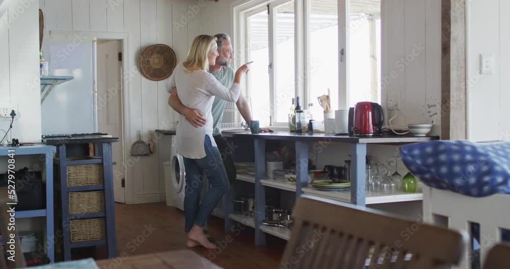 Happy caucasian mature couple drinking coffee and looking through the window in the kitchen Happy caucasian mature couple drinking coffee and looking through the window in the kitchen