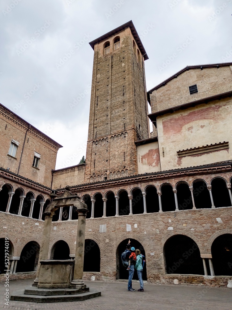 Unrecognizable tourist family with a man pointing to bell tower in Basilica Santuario Santo Stefano with Il Chiostro well courtyard