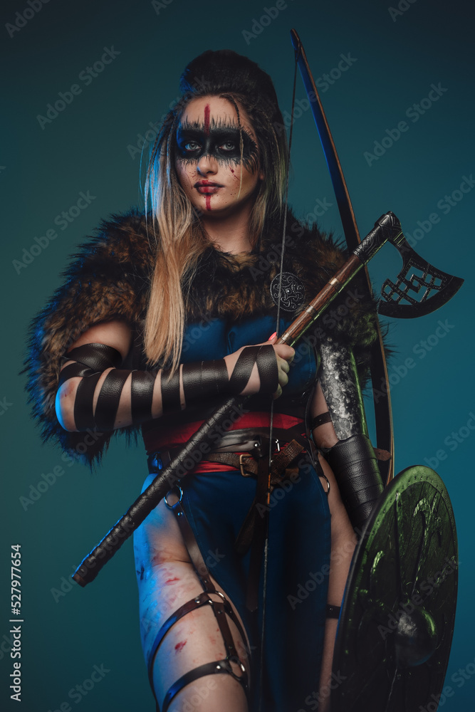 Photo of nordic huntress woman with strup back longbow holding shield and axe. Photo of nordic huntress woman with strup back longbow holding shield and axe.