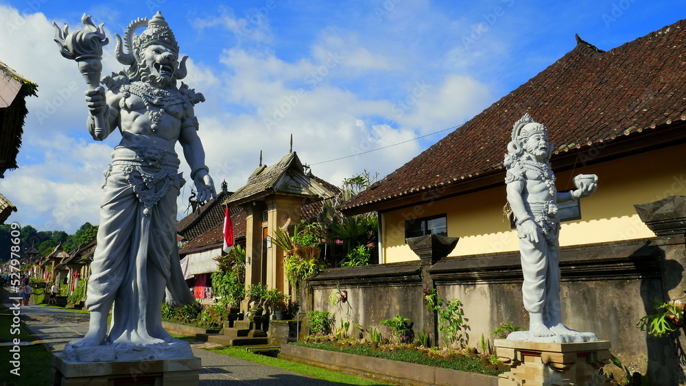 großen Skulpturen stehen entlang der Straße des  Dorfes Penglipuran in Bali mit traditionellen Häusern