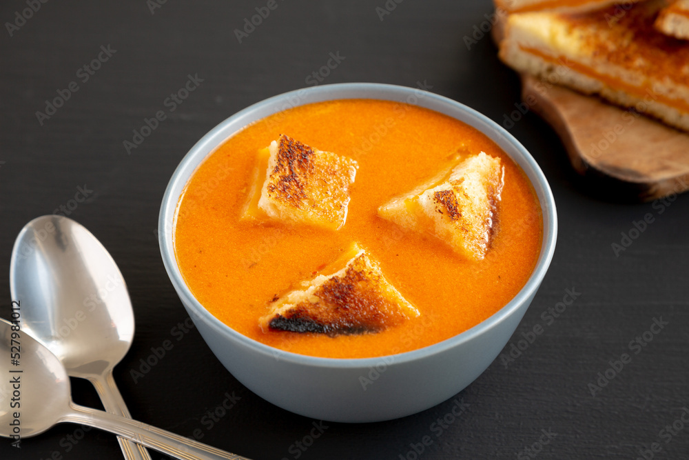 Homemade Tomato Soup with Grilled Cheese Croutons on a black background, side view. Homemade Tomato Soup with Grilled Cheese Croutons on a black background, side view.