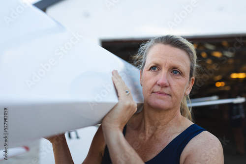 Senior caucasian female rower carrying boat on her shoulders to the lake photo