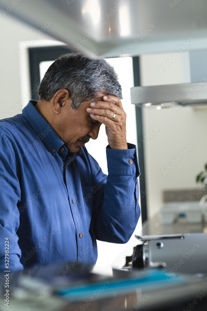 Senior mixed race man in kitchen holding his head in thought Senior mixed race man in kitchen holding his head in thought