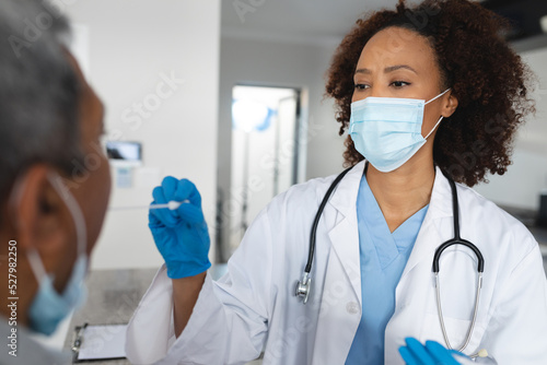 Mixed race female doctor wearing mask doing swab test on senior man at home photo
